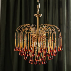 Modern brass chandelier with amber glass teardrop pendants on curved rods against dark curtains