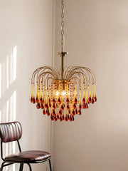 Modern brass chandelier pendant lamp with amber glass droplets hanging in minimalist room with leather chair
