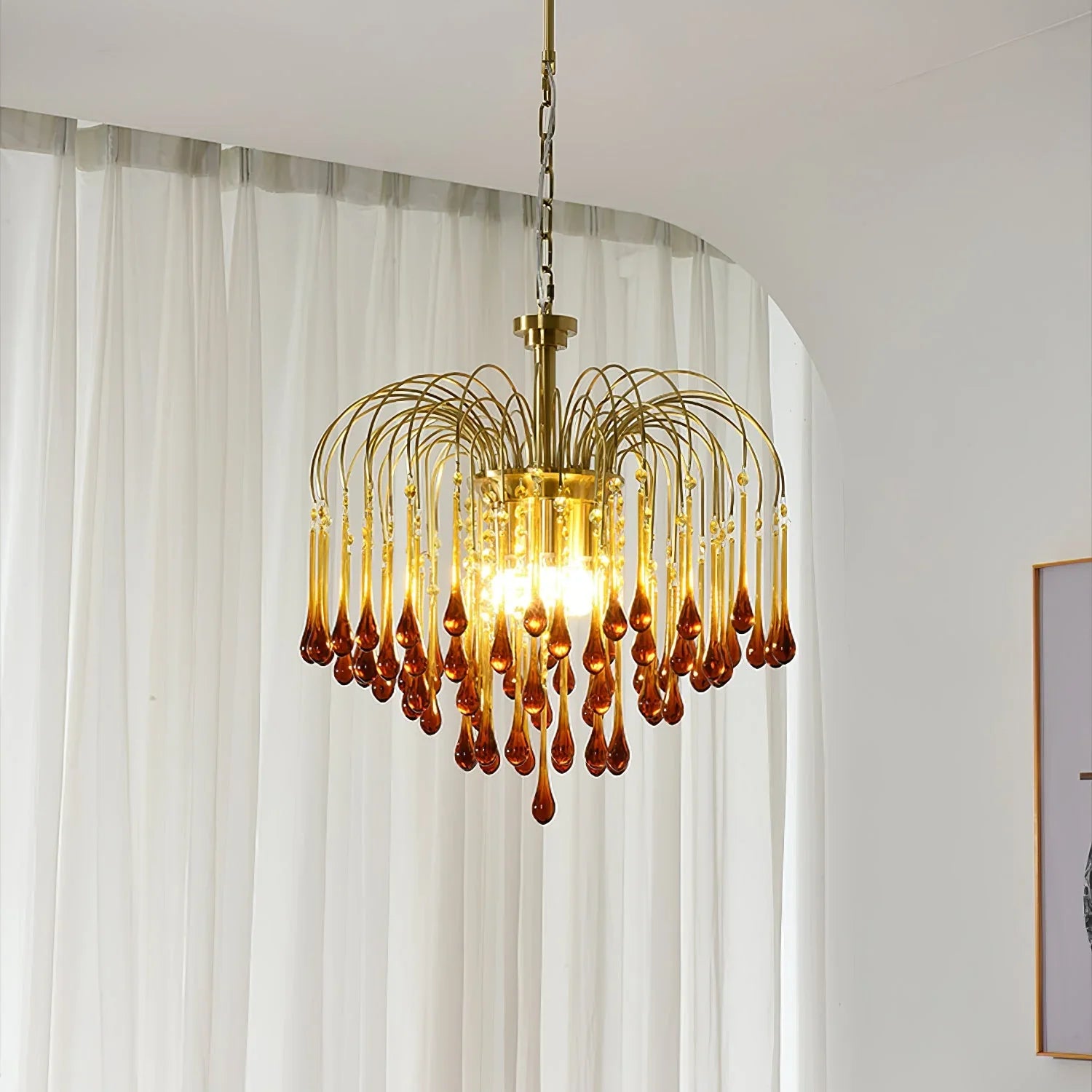 Modern brass chandelier pendant lamp with amber glass droplets hanging in bright room