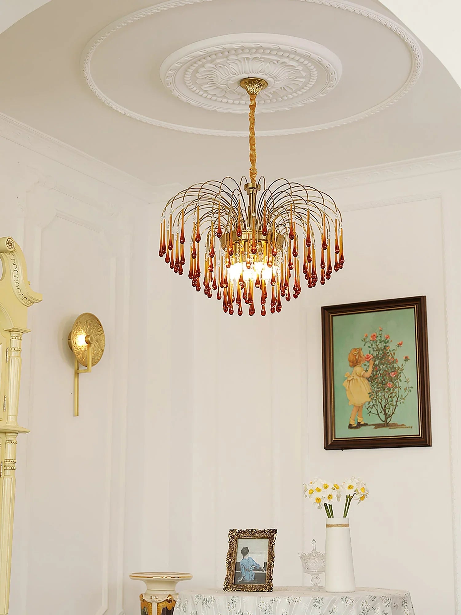 Modern brass chandelier with amber glass droplets hanging in classic white room with floral decor and framed art