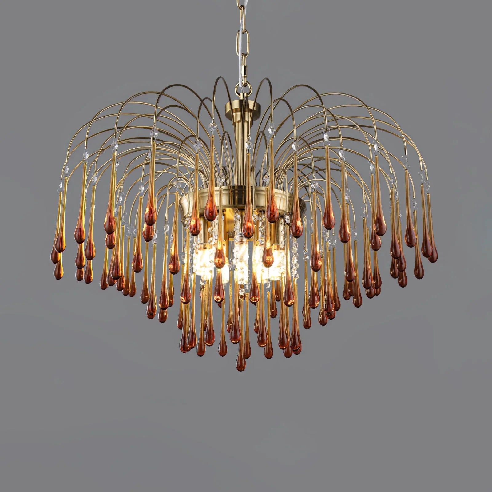 Modern brass chandelier with clear and amber maltose glass drops on curved metal arms against gray background