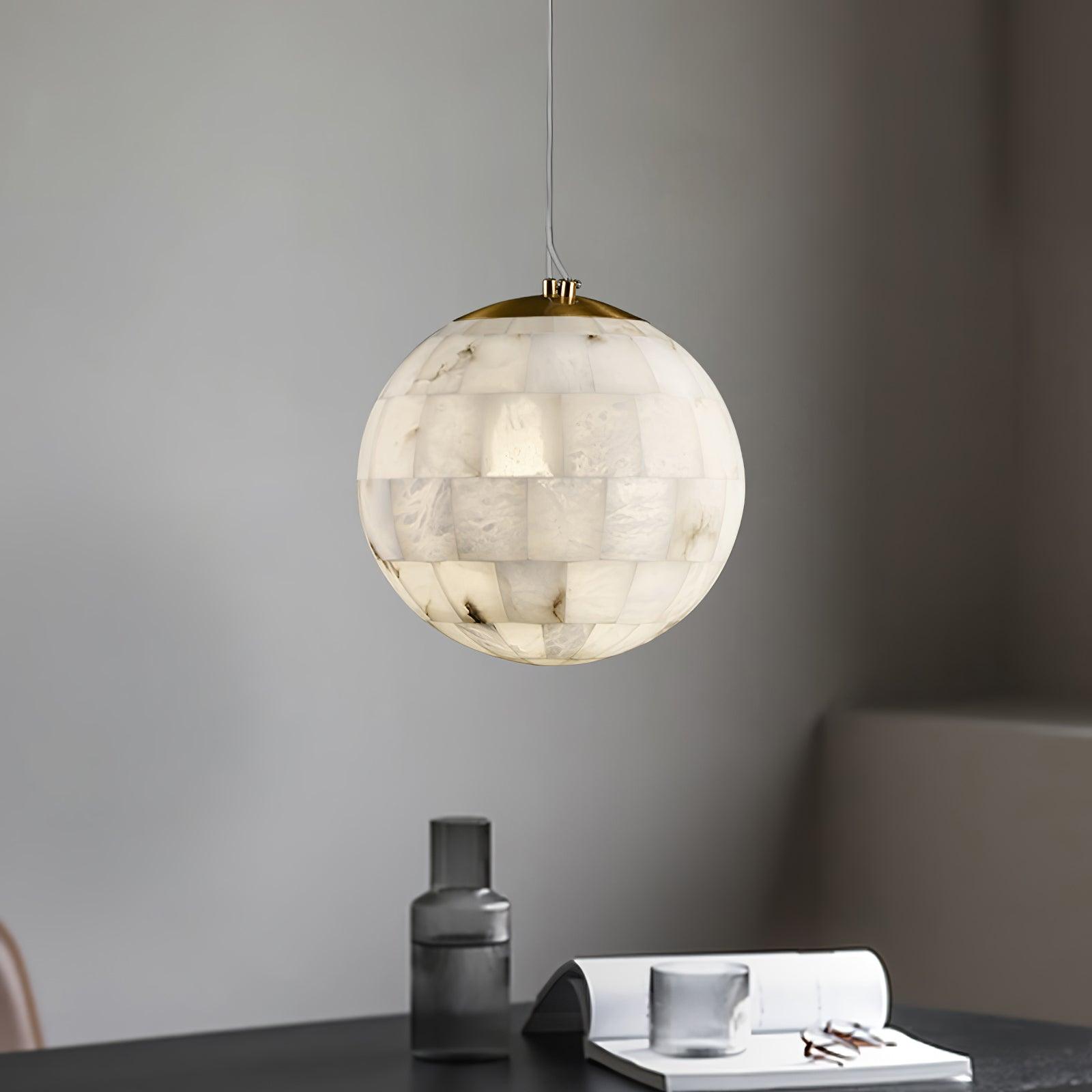 Modern spherical alabaster pendant lamp with brass top hanging over a black table with glassware and open book