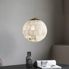 Modern spherical alabaster pendant lamp with brass top hanging over a black table with glassware and open book