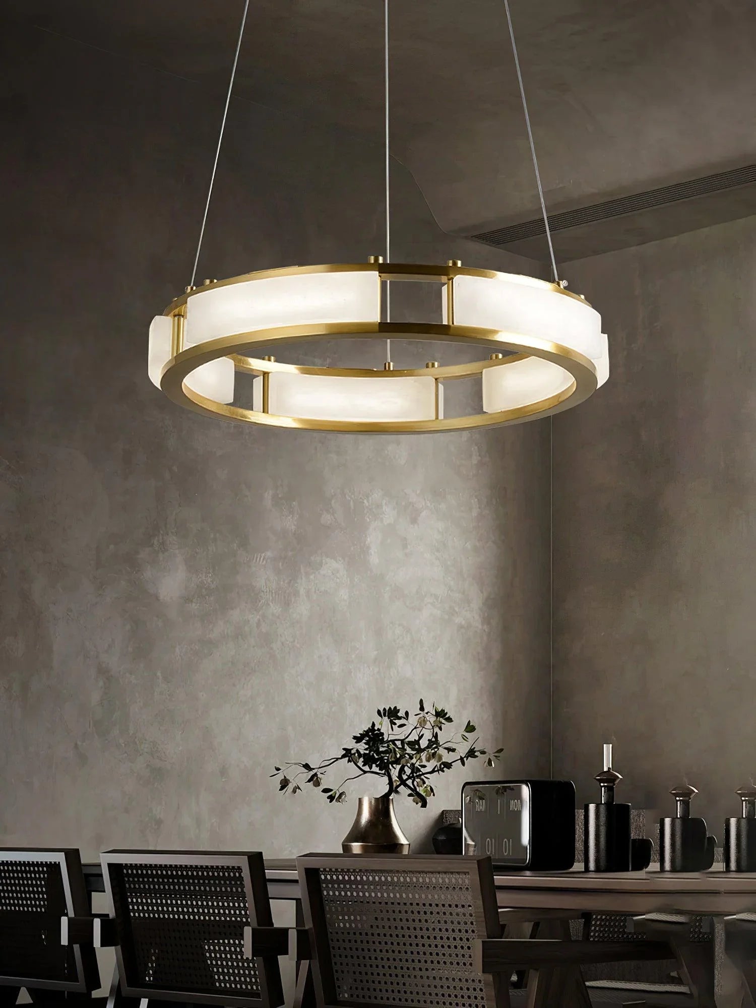 Modern brass and alabaster circular pendant chandelier hanging above dining table with dark chairs in minimalist room