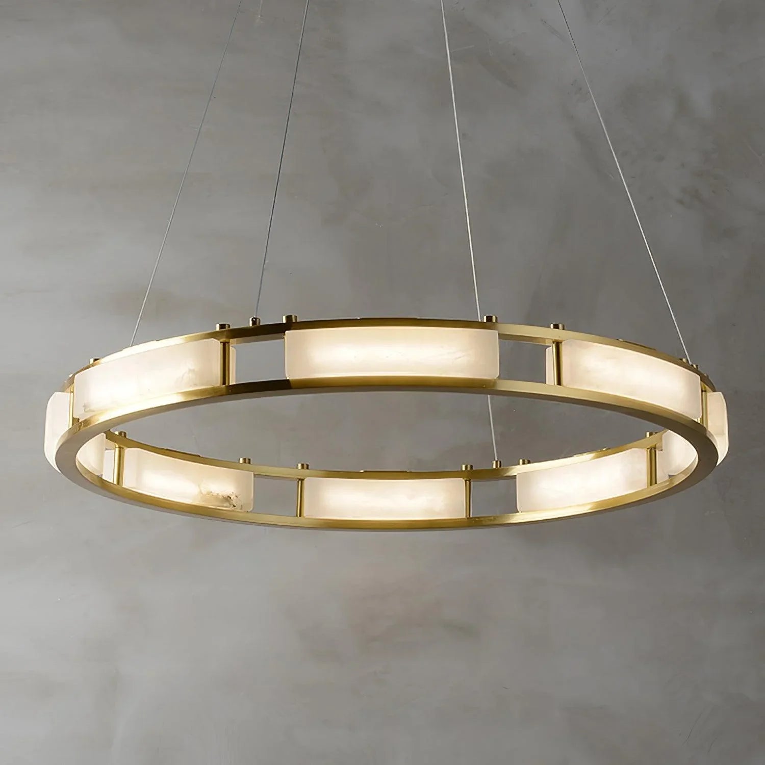 Modern brass round chandelier with alabaster panels and warm white light hanging against a gray wall