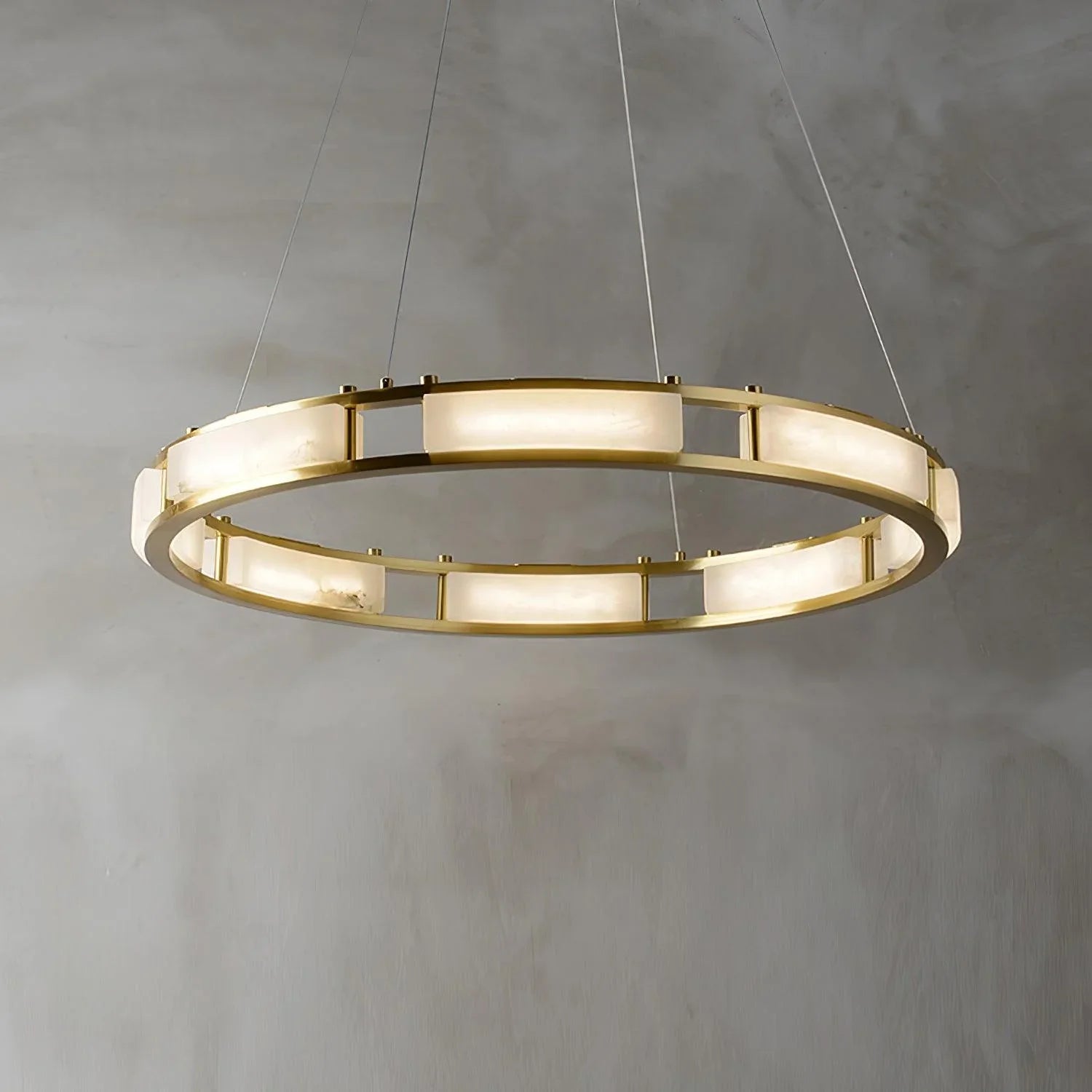 Modern round brass chandelier pendant lamp with alabaster light panels hanging against a gray wall