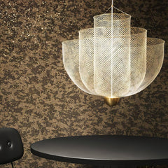 Modern gold-based pendant lamp with warm light mesh design hanging above black table and chair
