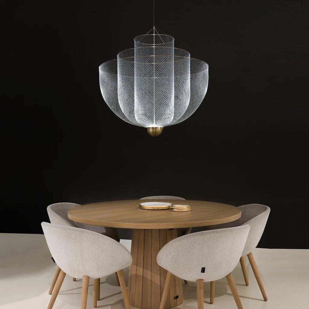 Modern pendant lamp with chrome mesh and gold base hanging above wooden round table with beige upholstered chairs