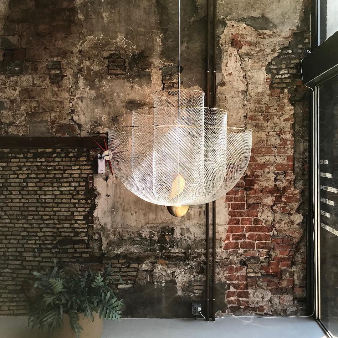 Modern chrome and gold mesh pendant chandelier with warm light against rustic exposed brick wall