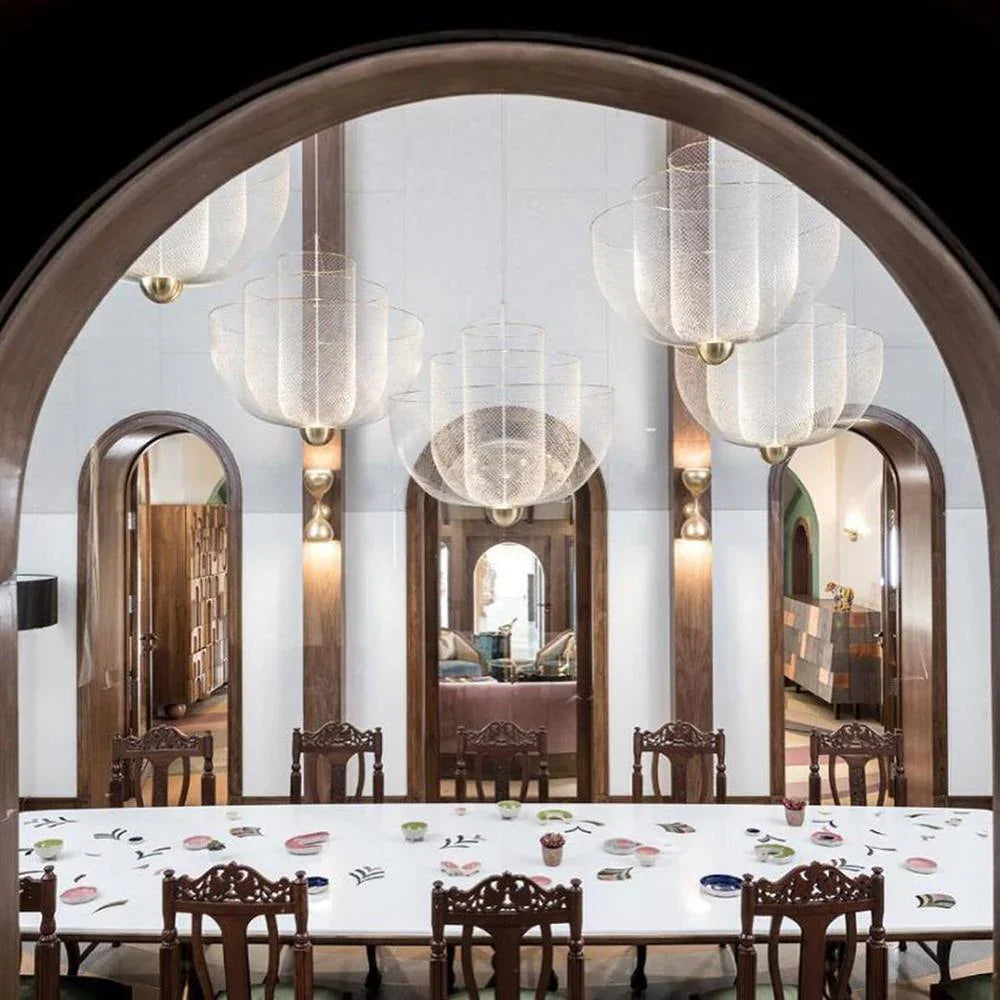 Elegant modern dining room with white table, ornate wooden chairs, and multiple mesh pendant chandeliers