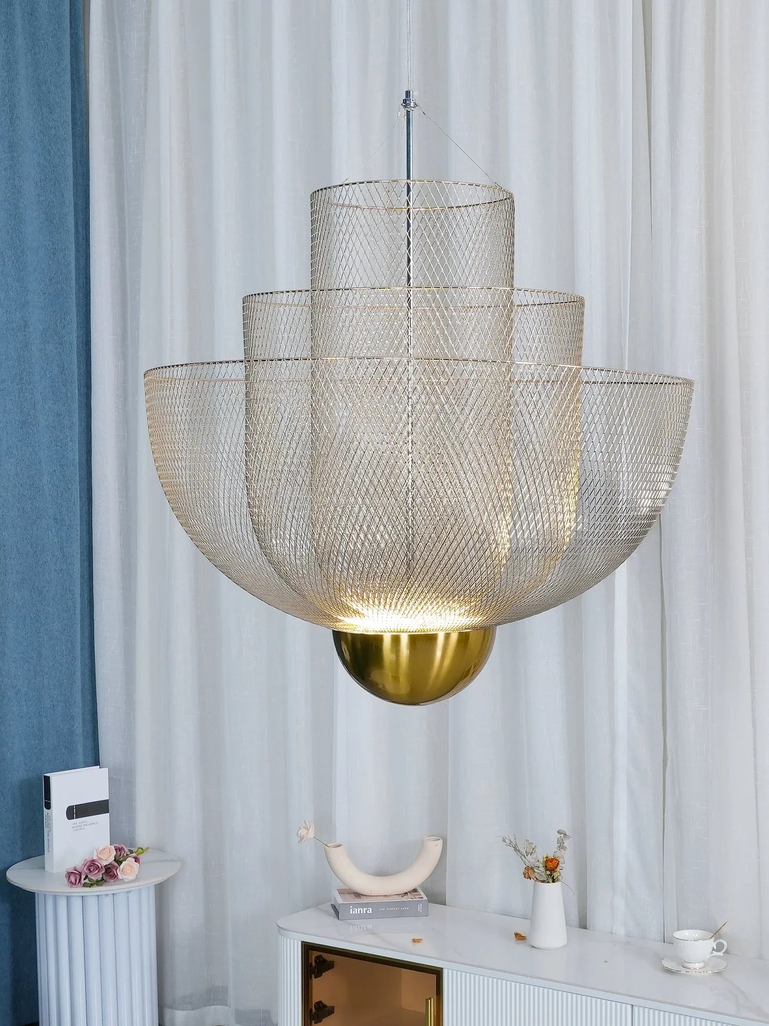 Modern pendant chandelier with layered gold mesh shades and a gold base, hanging over white marble console