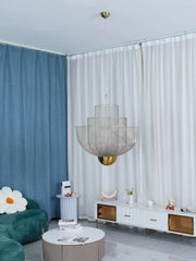 Modern mesh pendant chandelier with gold base hanging in stylish living room with blue and white curtains