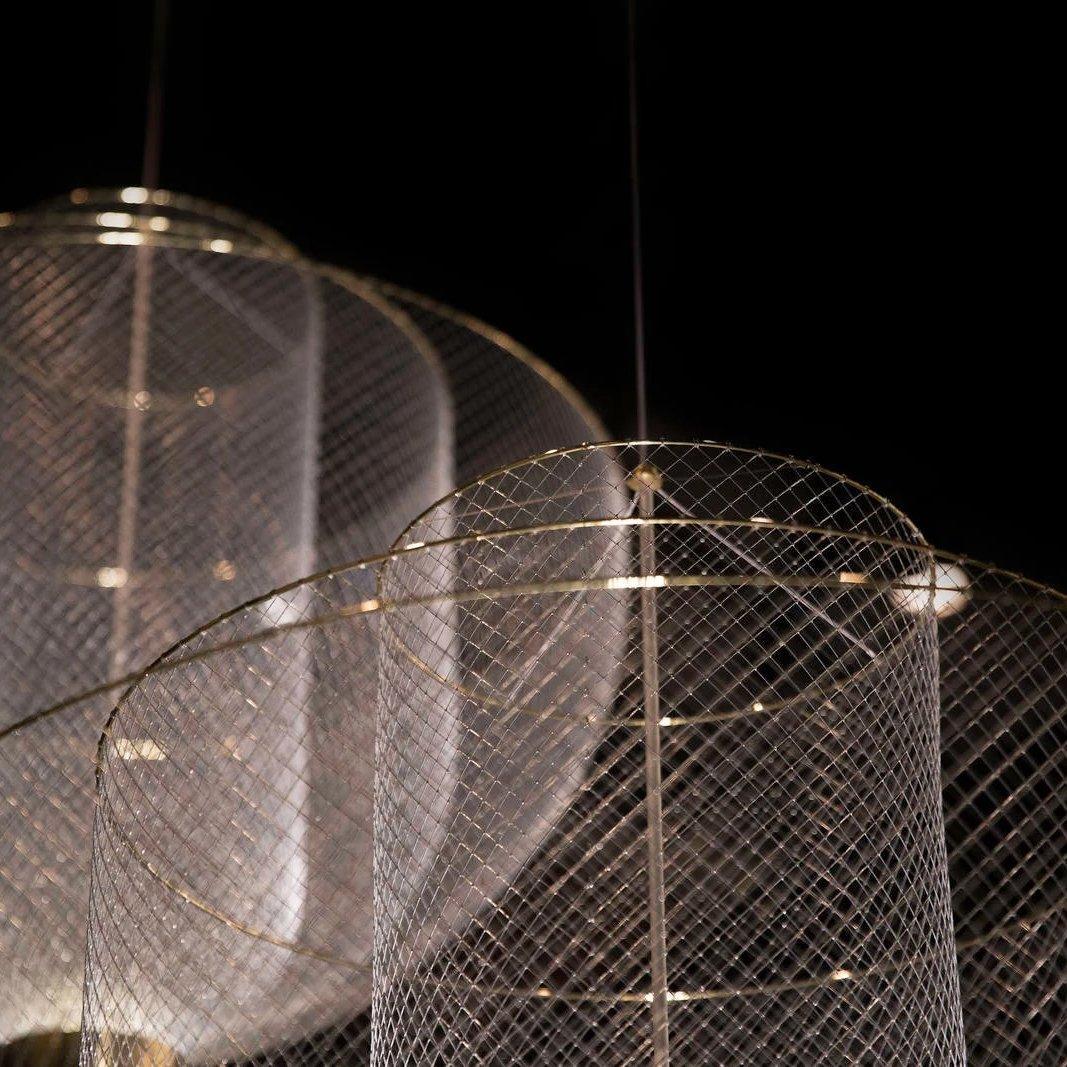 Modern pendant lamp with gold base and mesh cylindrical shade hanging against black background