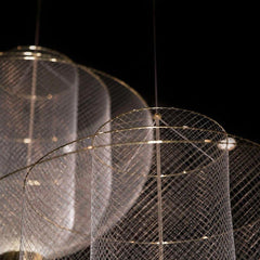 Modern pendant lamp with gold base and mesh cylindrical shade hanging against black background