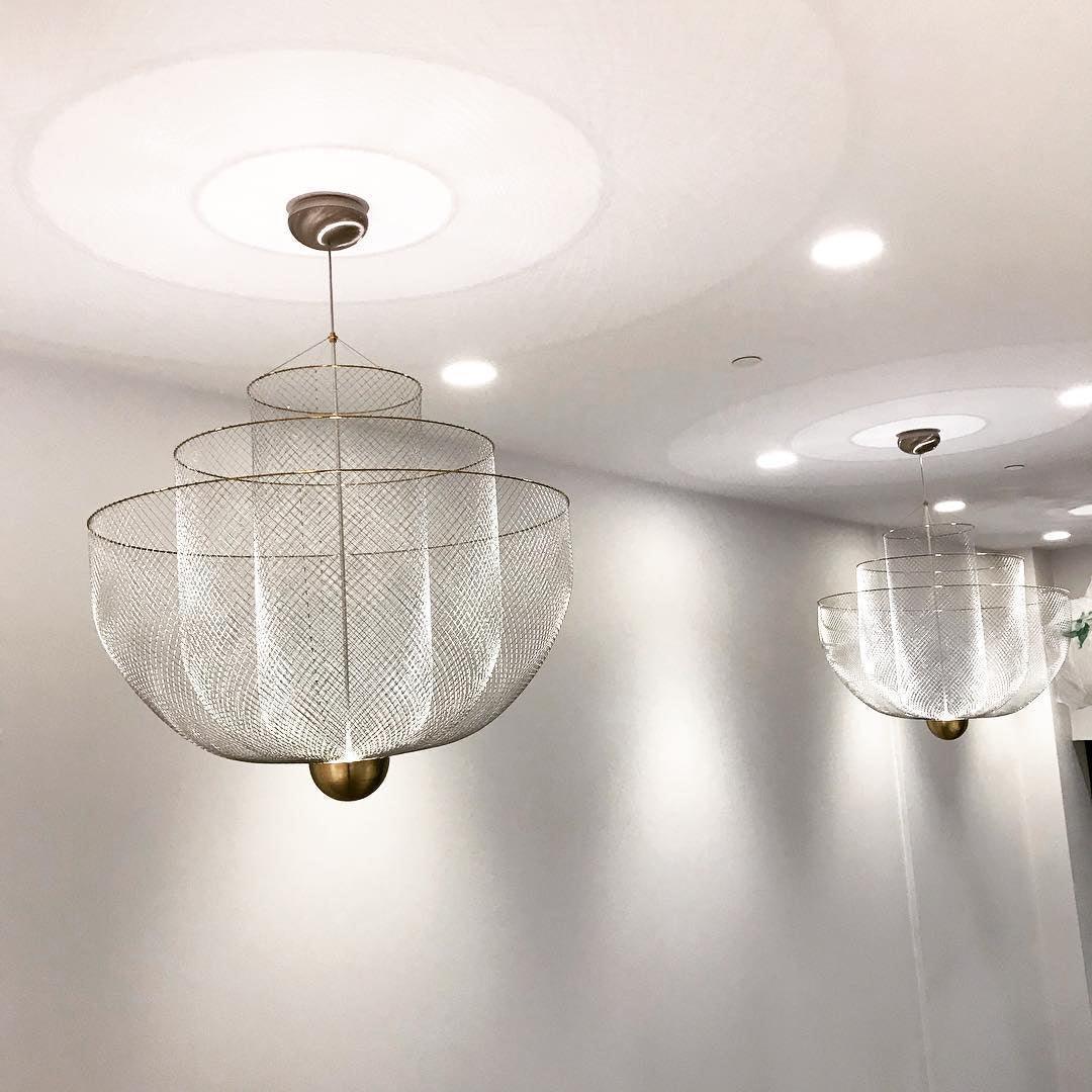 Modern mesh pendant chandeliers with chrome bodies and gold bases hanging from a white ceiling in a minimalist room