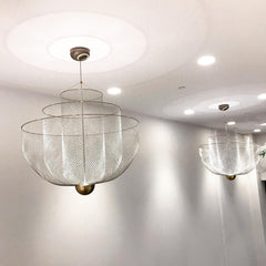 Modern mesh pendant chandeliers with chrome bodies and gold bases hanging from a white ceiling in a minimalist room