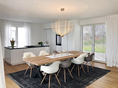 Modern dining room with wooden table, mixed white and gray chairs, black rug, and gold-base mesh pendant chandelier