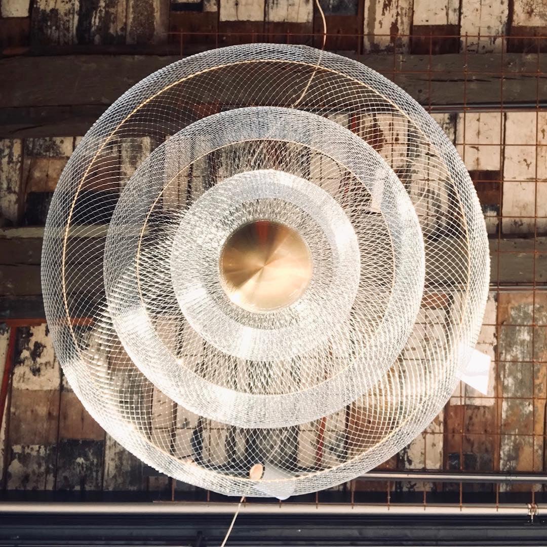 Modern gold and chrome pendant chandelier with concentric mesh rings, suspended against rustic ceiling