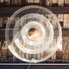 Modern gold and chrome pendant chandelier with concentric mesh rings, suspended against rustic ceiling