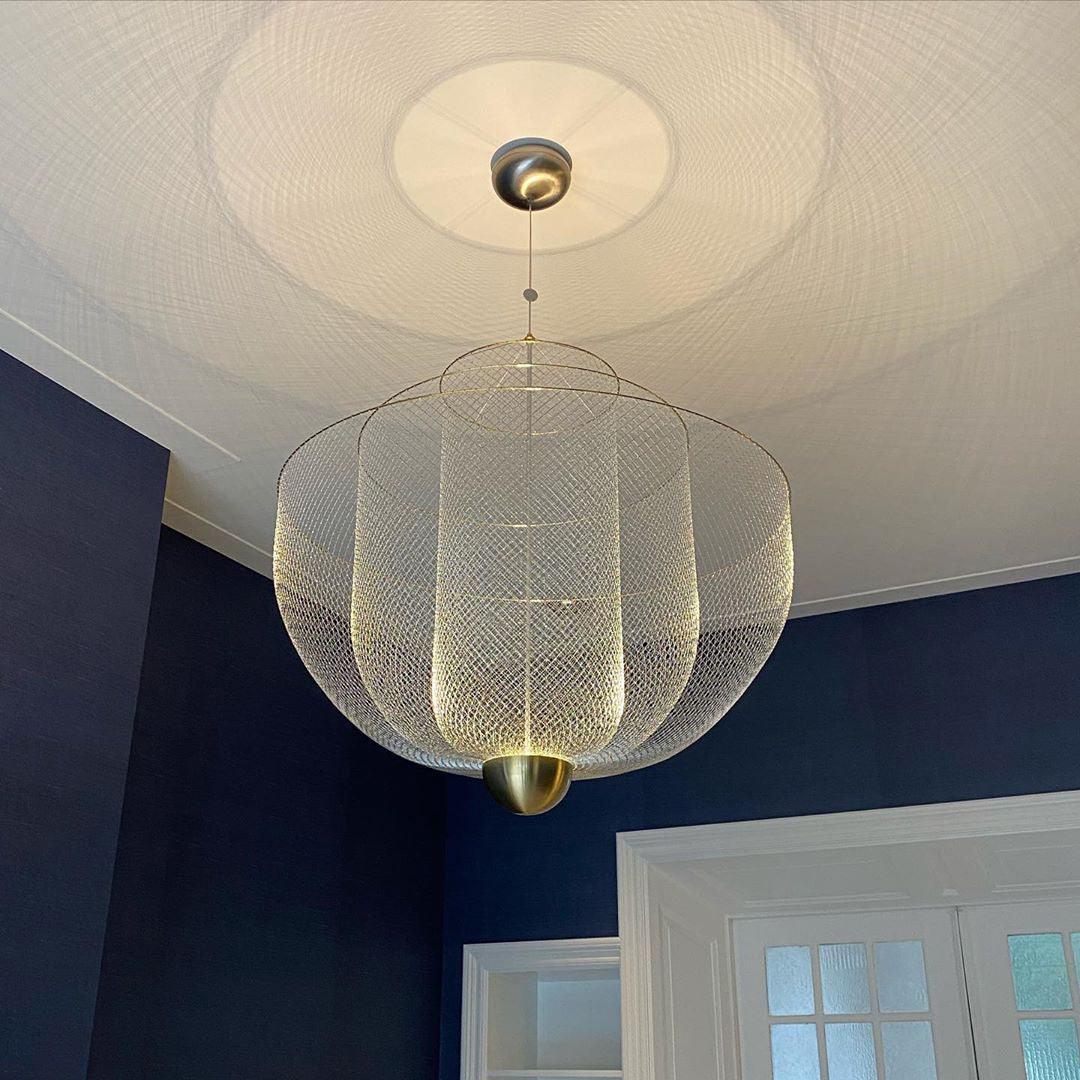 Modern pendant lamp with gold base and chrome mesh shade casting patterned light in a stylish room