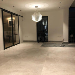 Modern chrome and gold mesh pendant chandelier hanging in minimalist room with large beige tile floor