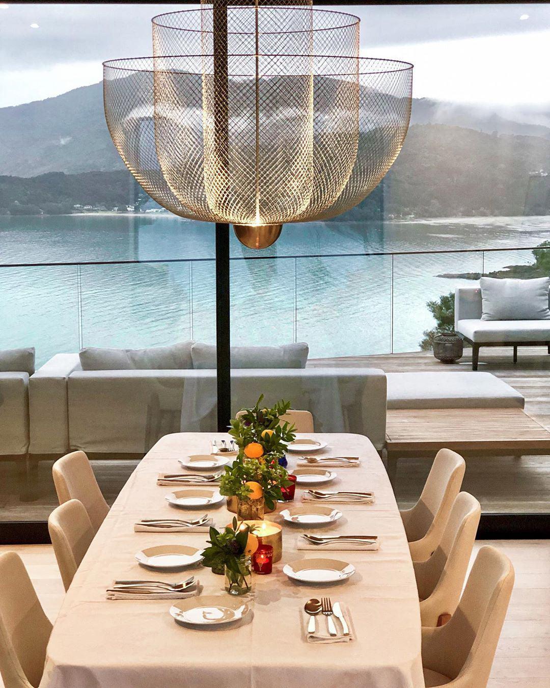 Modern dining room with white tablecloth, set table, and large gold mesh pendant chandelier overlooking lake view