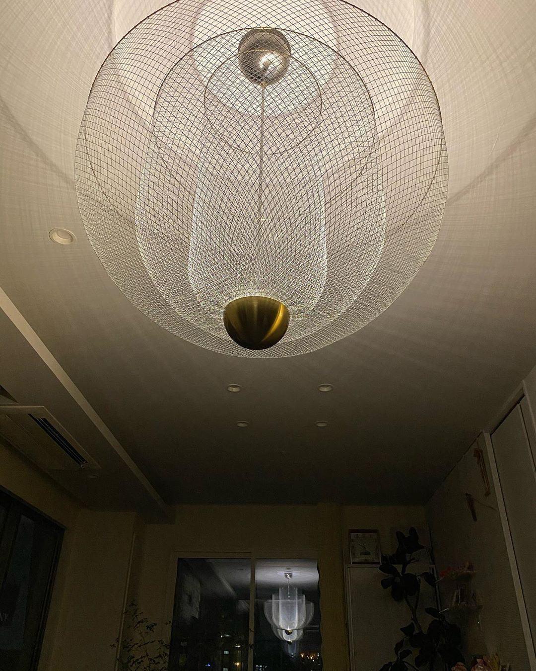 Modern pendant chandelier with chrome mesh and gold base casting intricate shadows on ceiling in cozy room