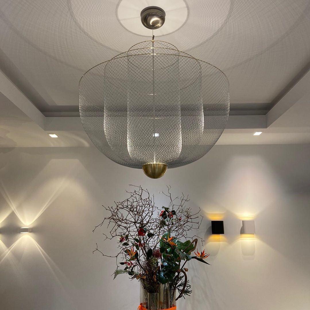 Modern mesh pendant lamp with gold base hanging from ceiling above floral arrangement in a minimalist room