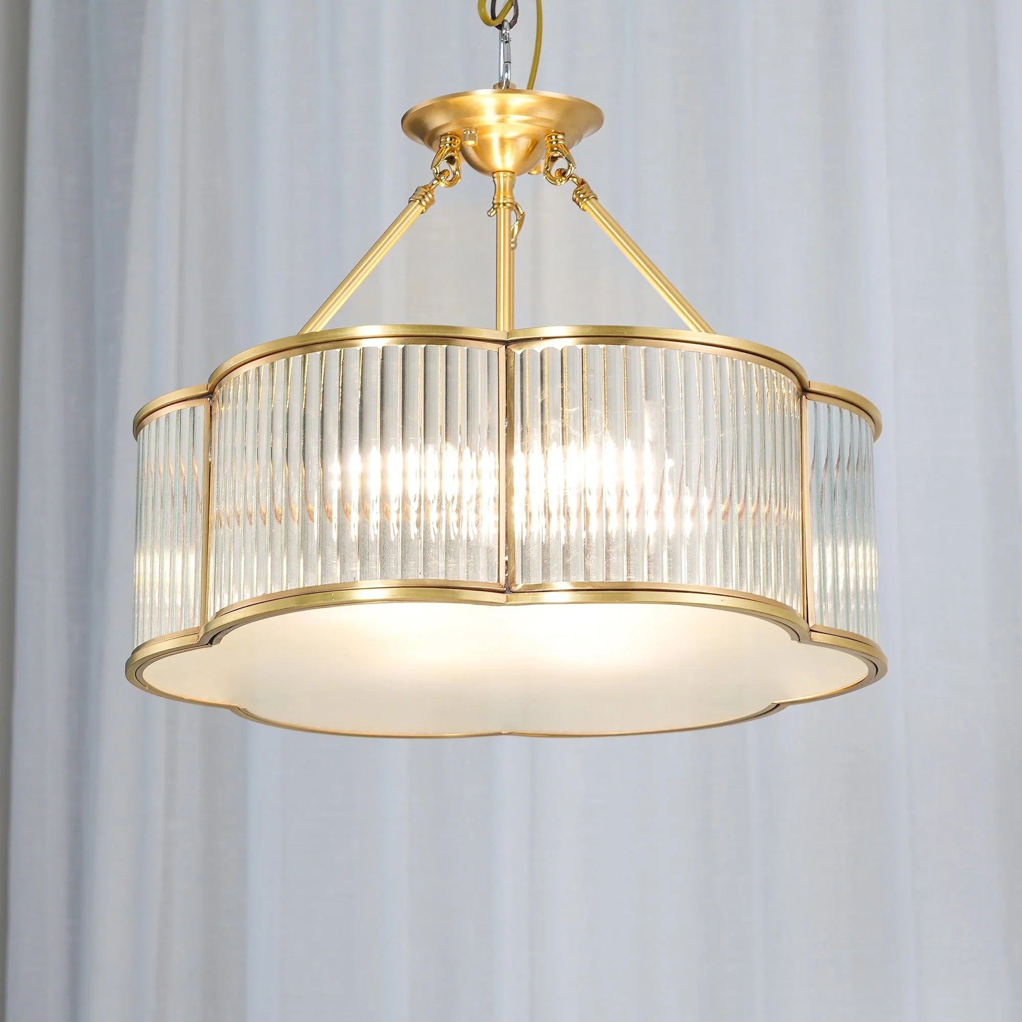 Modern brass pendant chandelier with glass panels from YH Lamps, illuminated against white curtains