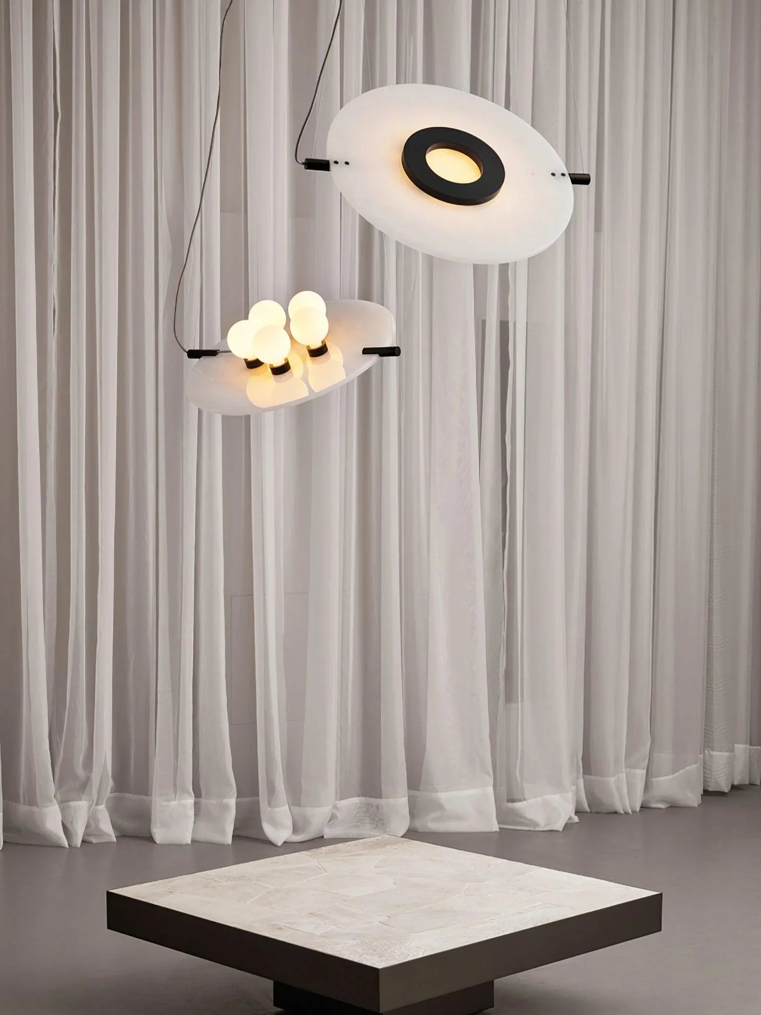 Modern pendant lamp with circular white shades and black accents hanging in a minimalist room with sheer curtains
