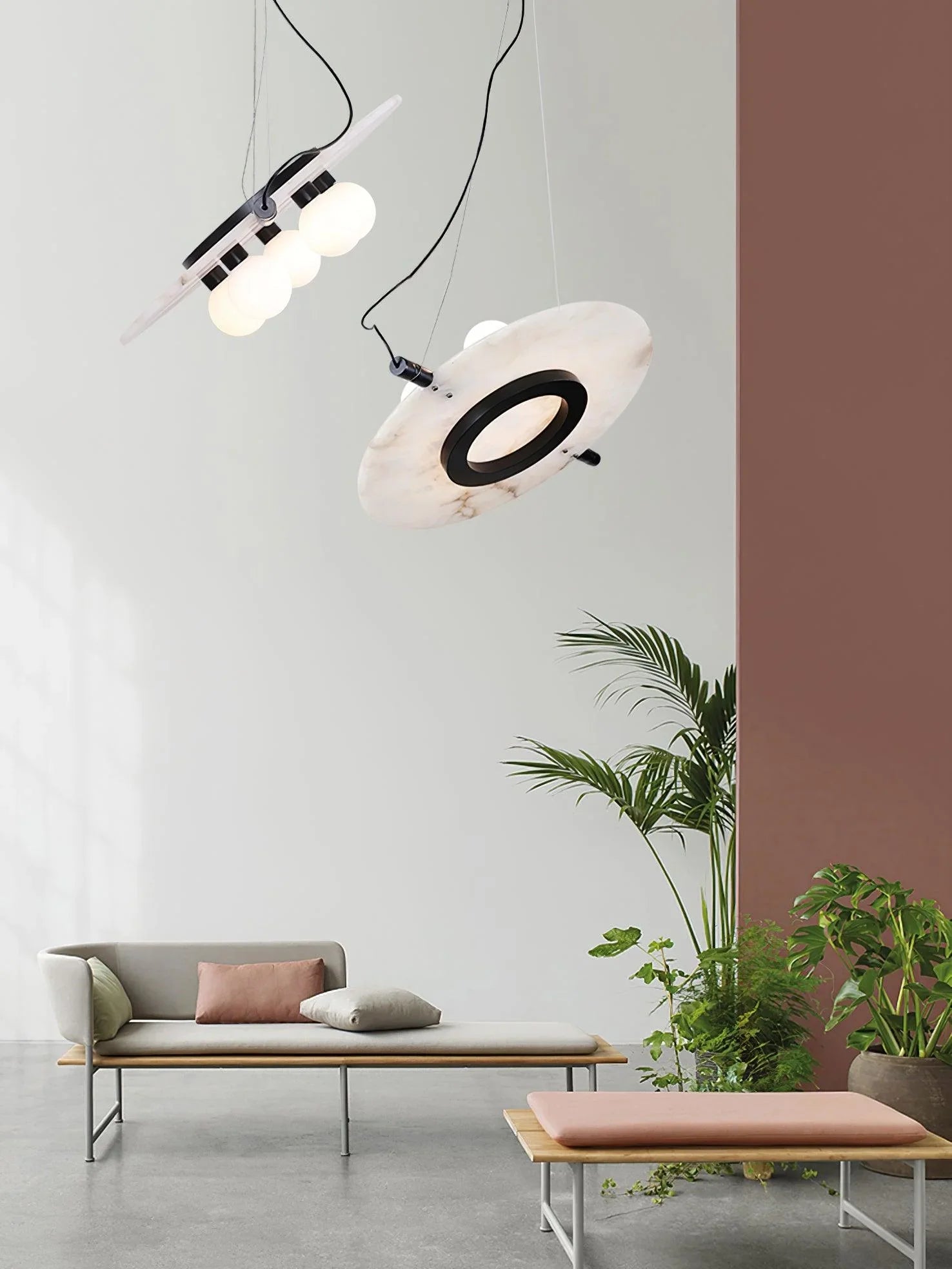 Modern pendant chandelier with black and white marble discs lighting a minimalist living space with neutral sofa and green plants