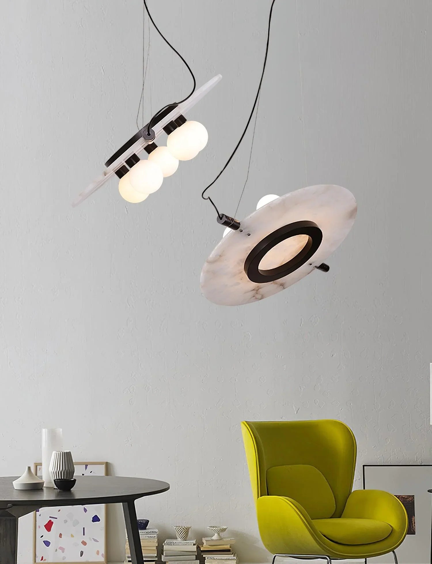 Modern pendant lamps with spherical bulbs and marble-like disc shades above a round black table and lime green armchair