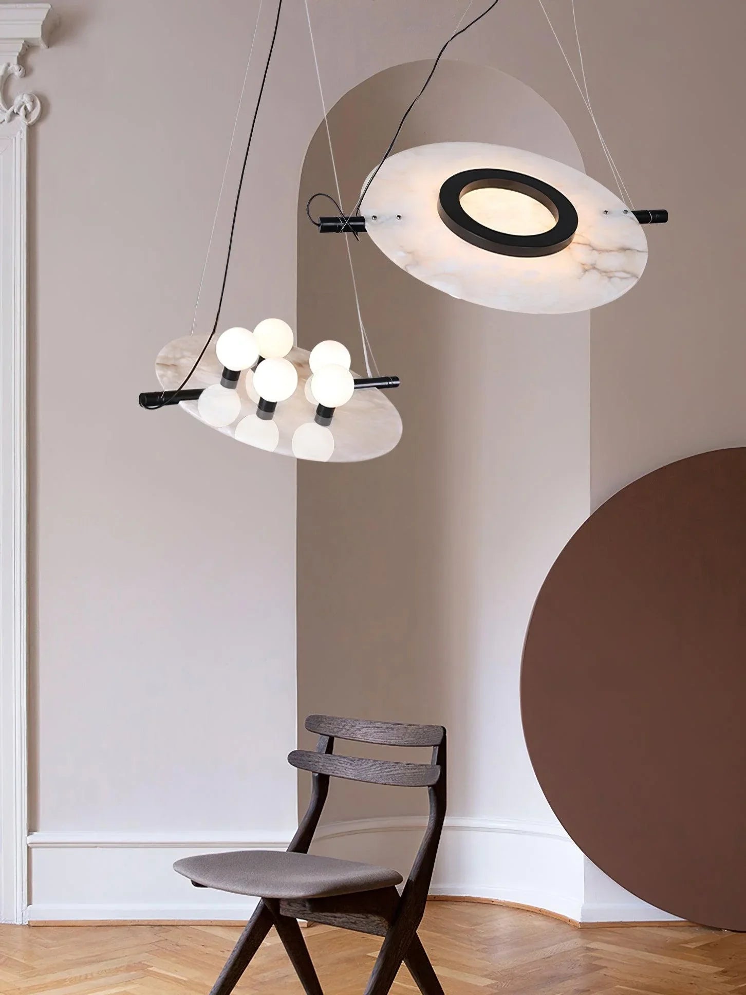 Modern pendant lamp with white marble discs and black accents above a dark wood chair in a minimal beige room
