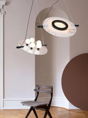 Modern pendant lamp with white marble discs and black accents above a dark wood chair in a minimal beige room