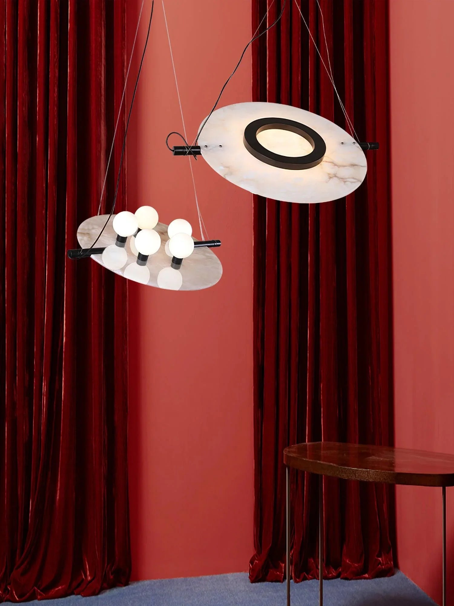 Modern pendant chandelier with white marble discs and multiple round bulb lights, against red velvet curtains