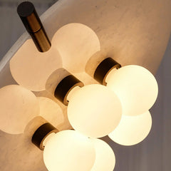 Modern wall sconce with four glowing round white glass bulbs and black mounts on textured wall