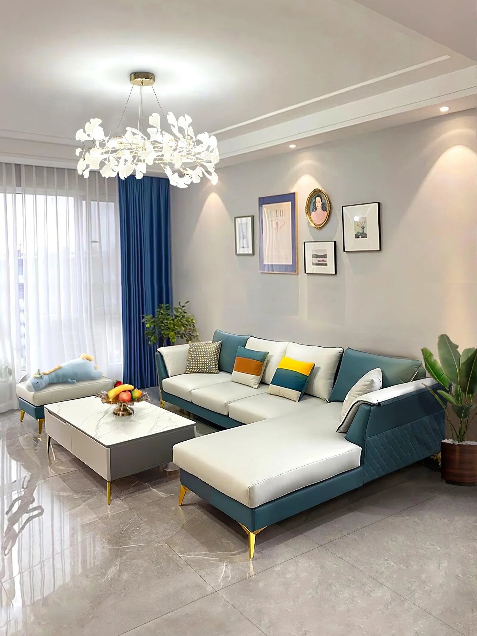 Modern living room with white and teal sectional sofa, colorful pillows, marble coffee table, and white gingko chandelier