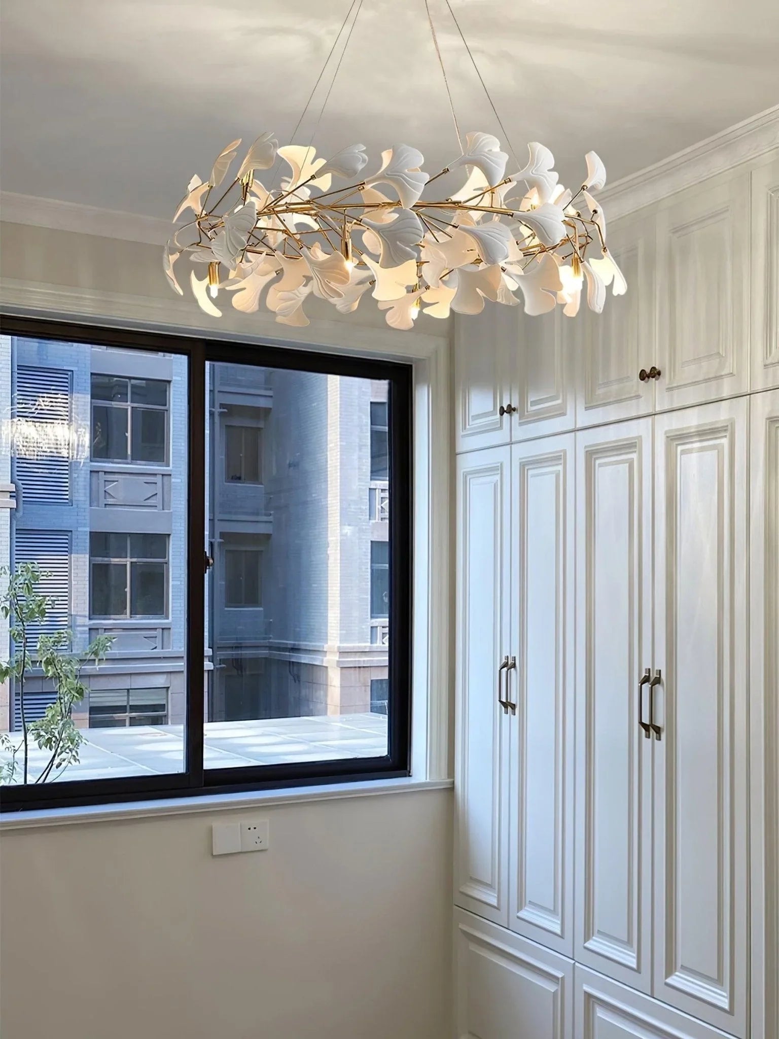 Modern gold and white ginkgo leaf chandelier pendant lamp in elegant room with white cabinets and large window