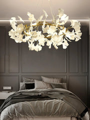 Modern gold and white ginkgo leaf chandelier pendant lamp over a gray bed in a stylish bedroom with dark paneled wall