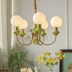 Modern gold and green chandelier with five frosted globe lights hanging in a bright room with yellow flowers and framed art