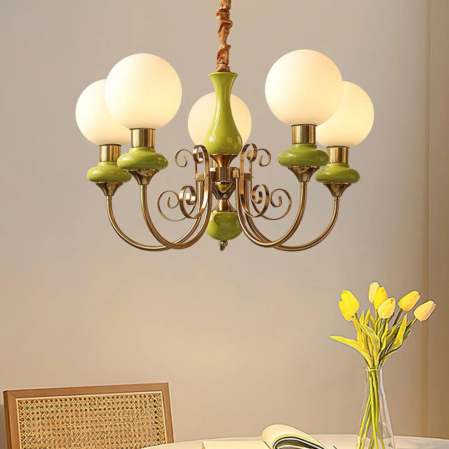 Modern chandelier with five frosted globe lights and green gold metal arms above dining table with yellow tulips