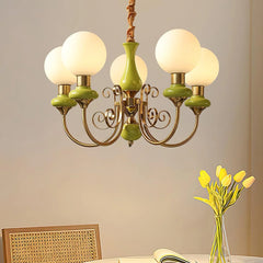 Modern chandelier with five frosted globe lights and green gold metal arms above dining table with yellow tulips