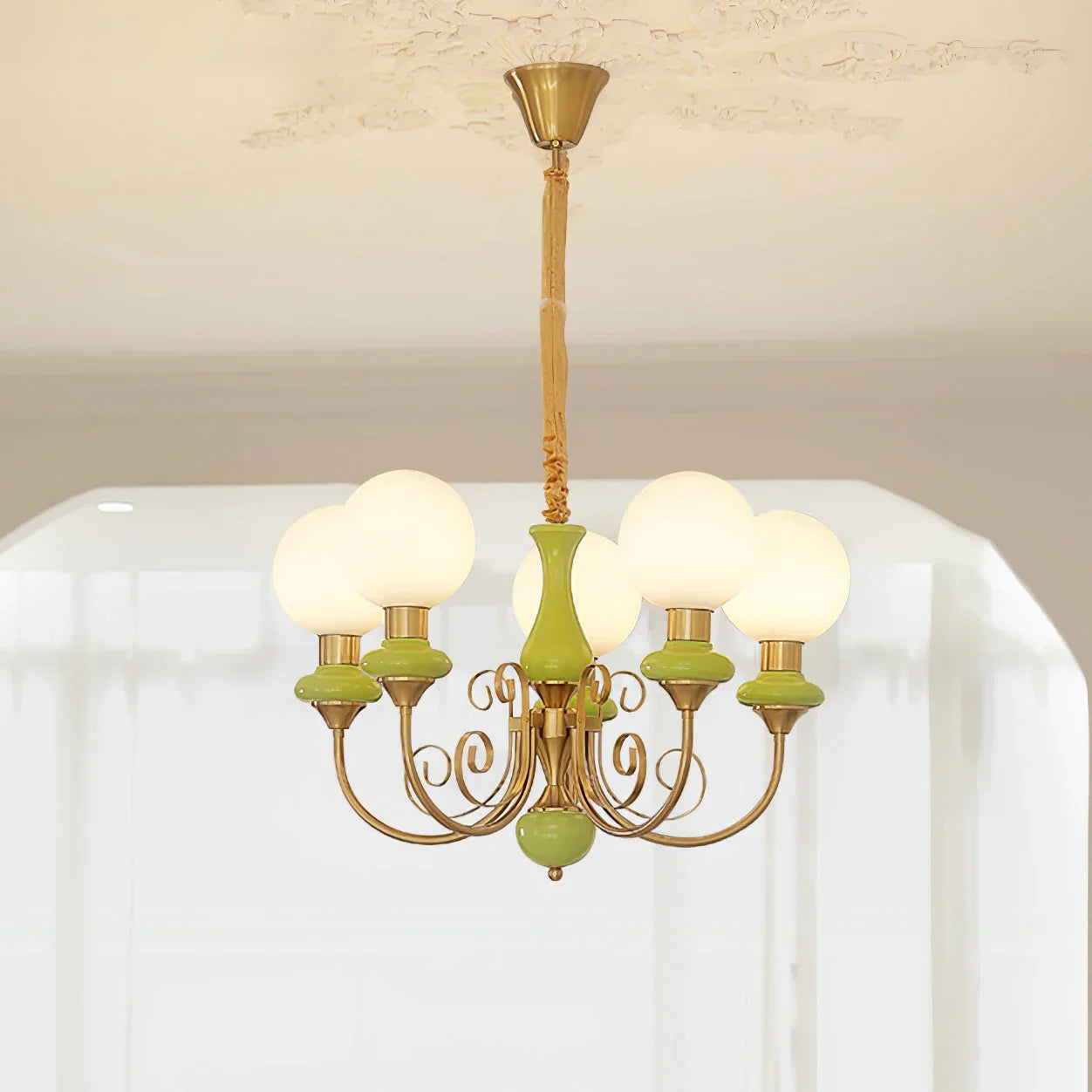 Modern chandelier with six white globe lights and green gold metal arms hanging from decorated ceiling