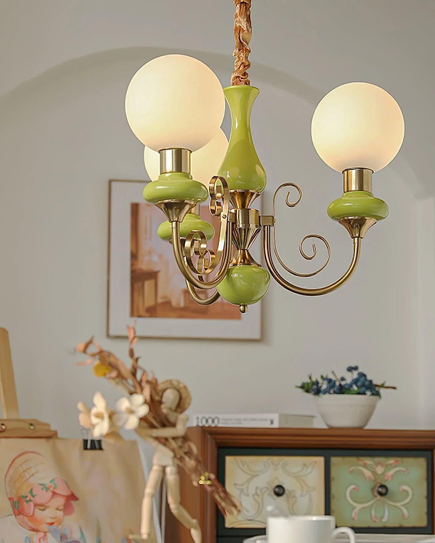 Modern chandelier with three round white glass shades and gold green metal accents hanging in cozy room