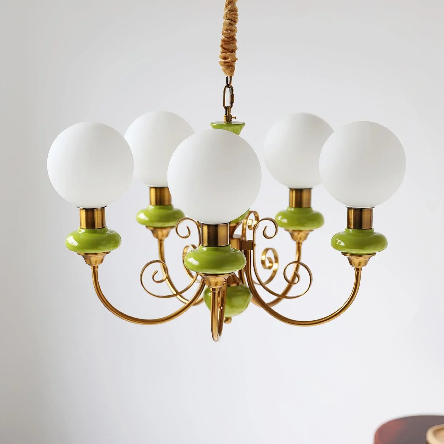 Modern chandelier with five white globe lamps, gold arms, and green accents, hanging against white wall
