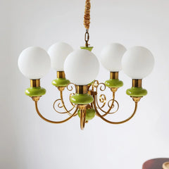 Modern chandelier with five white globe lamps, gold arms, and green accents, hanging against white wall