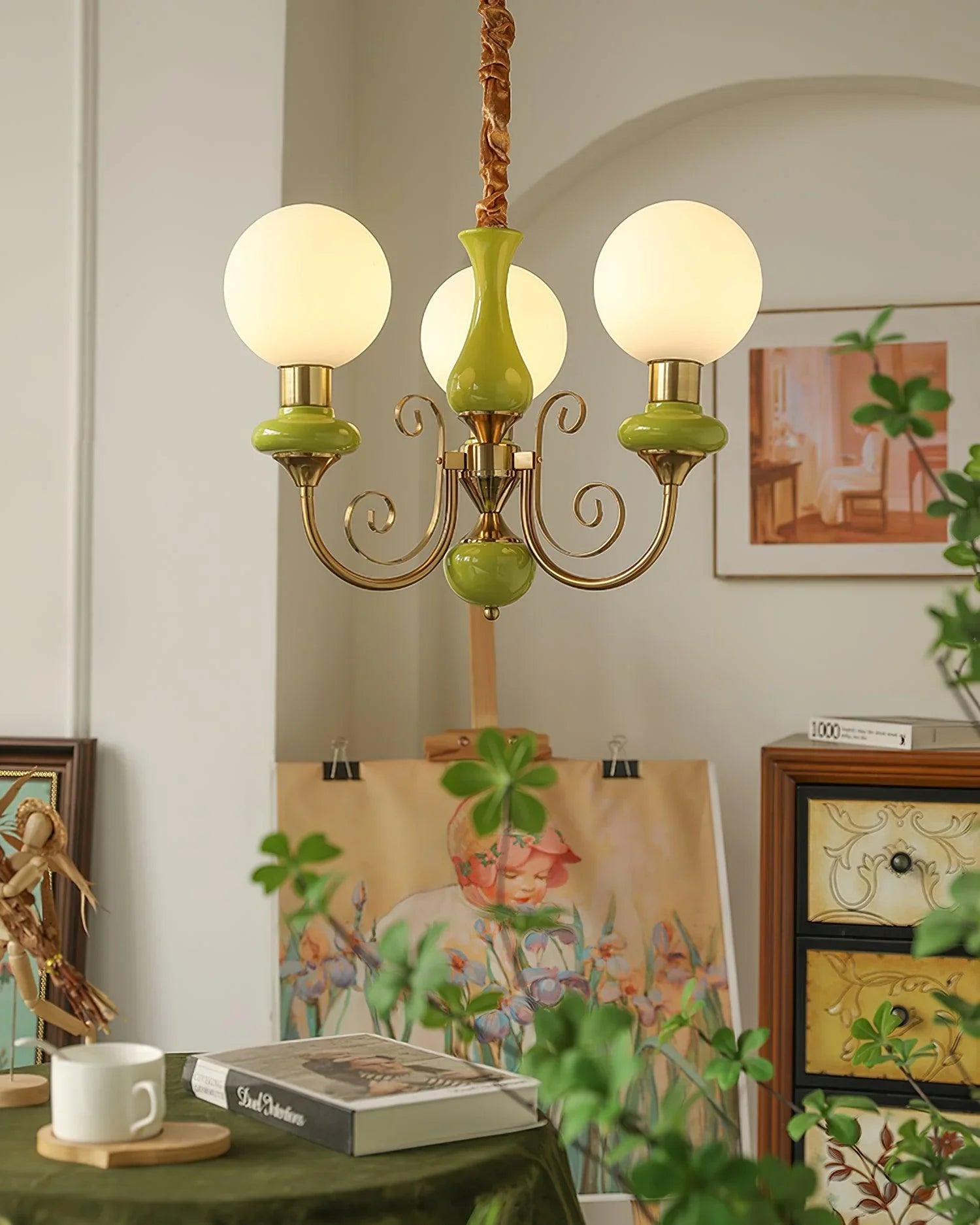 Modern 3-head pendant chandelier with gold and green accents hanging in cozy room with art, books, plants