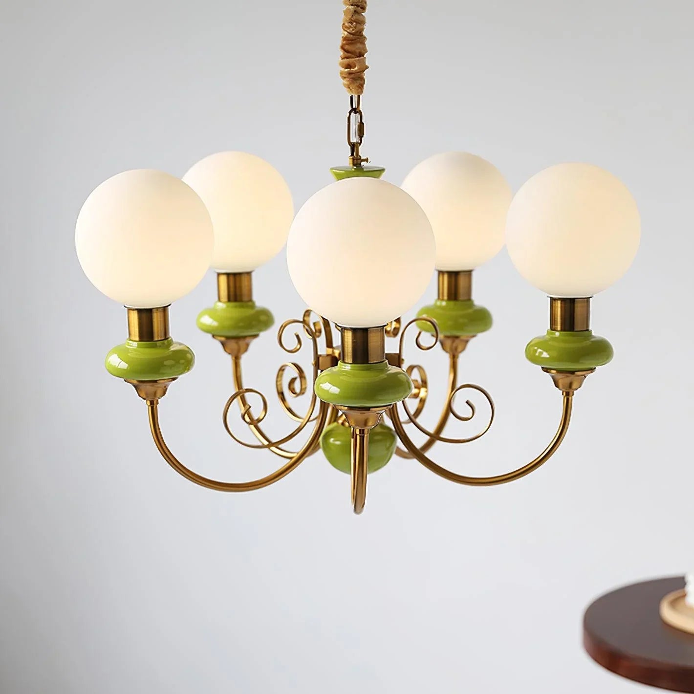 Modern chandelier with five white globe lamps, gold metal arms, and green accents hanging in a bright room