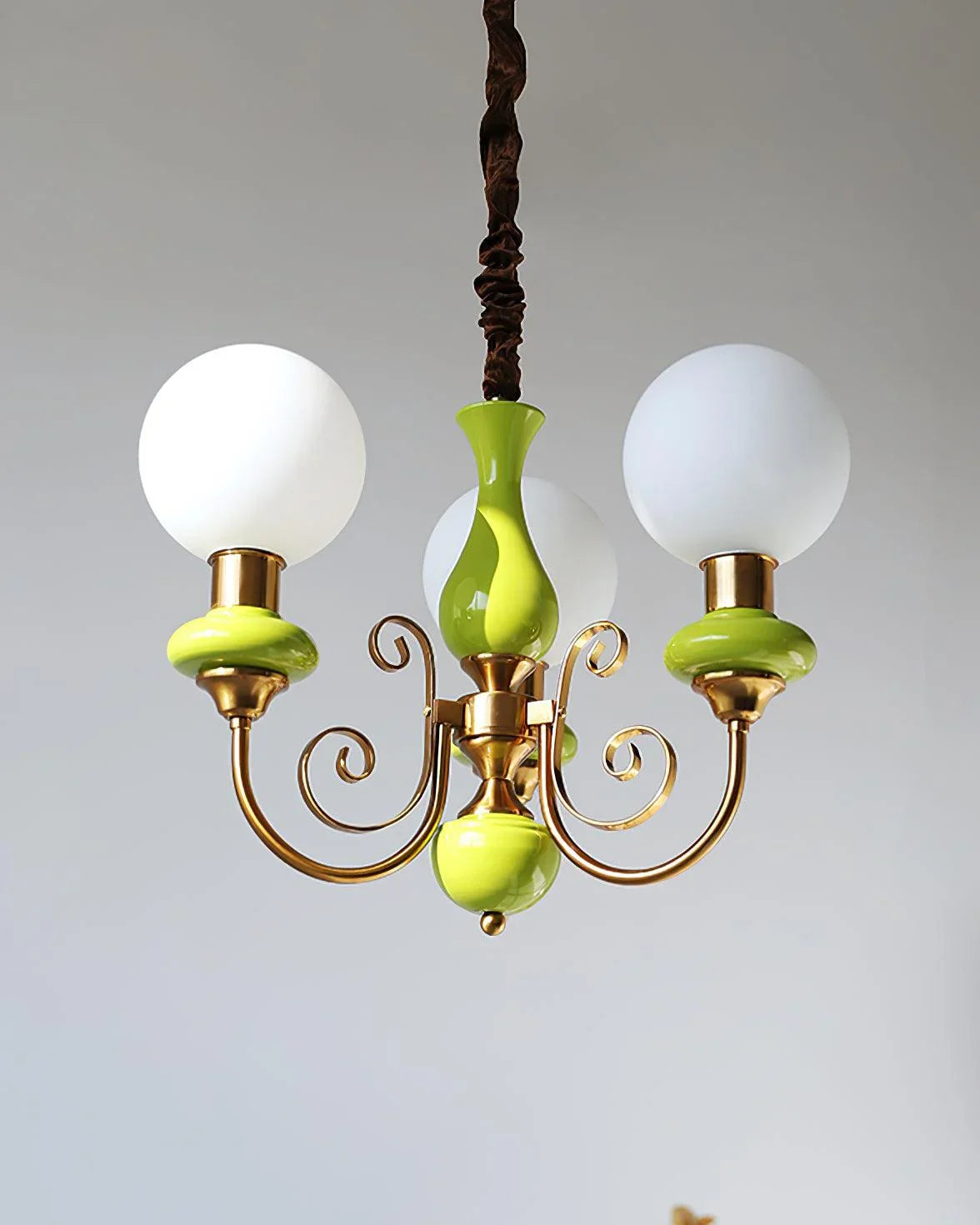 Modern chandelier with three frosted white globes and gold green metal accents hanging against gray background
