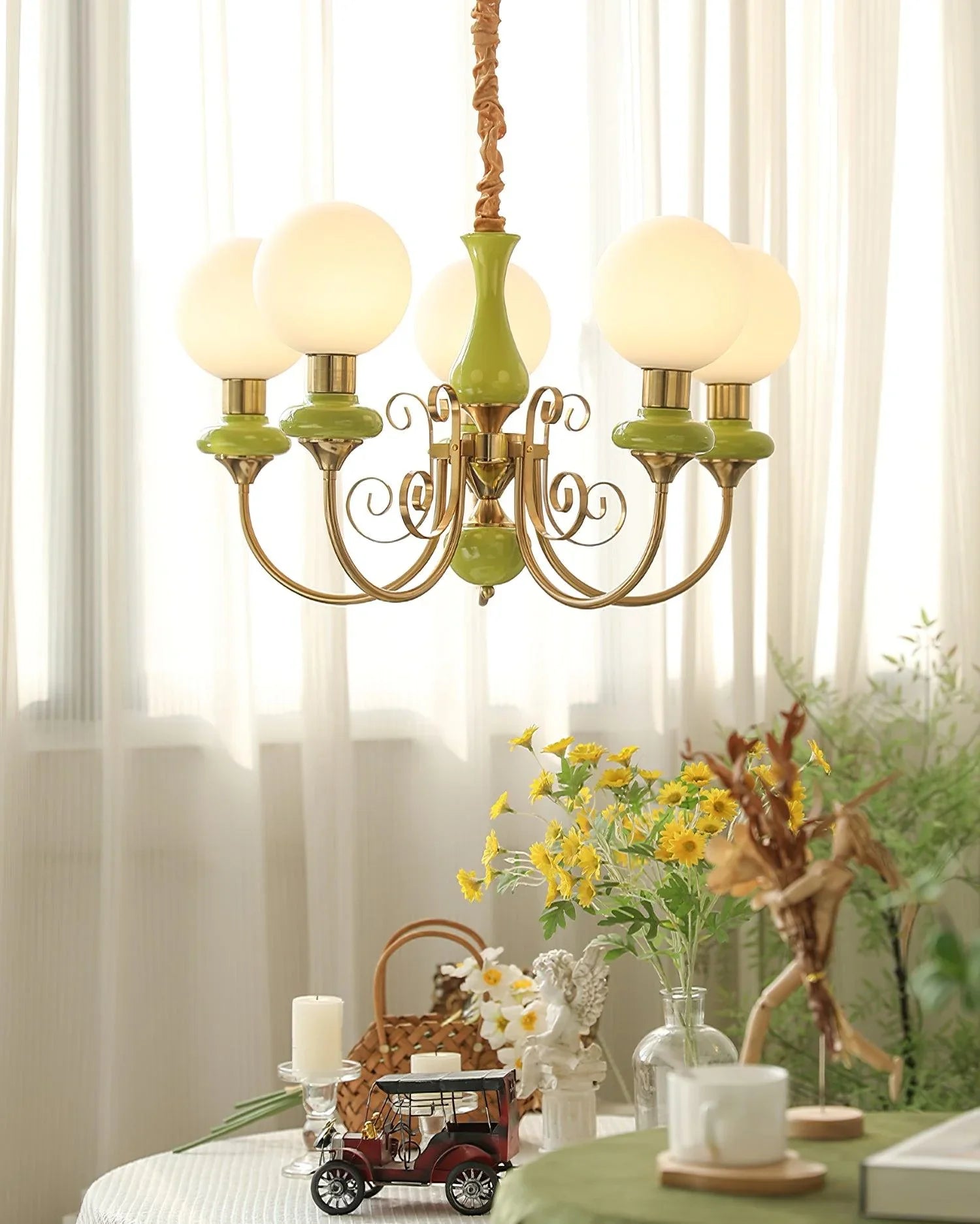 Vintage chandelier with green and gold accents and frosted glass globe lamps over a table with flowers and decor
